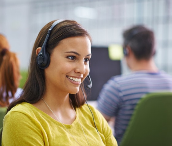 A woman wearing a computer headset discusses Rimini Support for Oracle Agile PLM